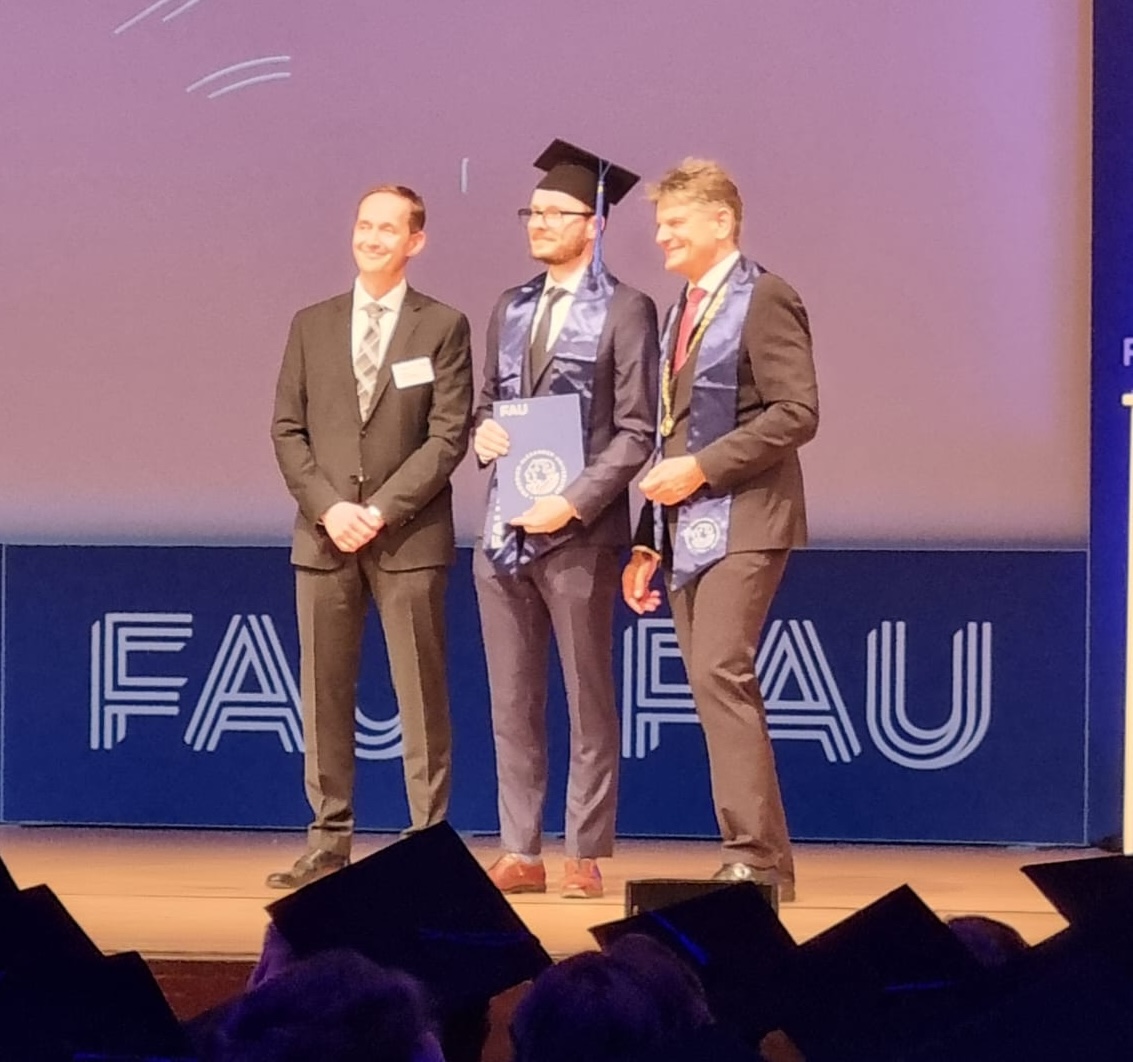 The image shows the author, a professor and the president of the university on stage at an university event.